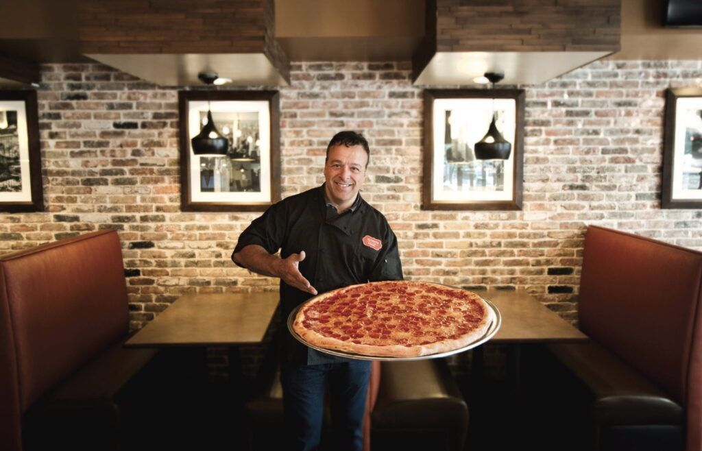 Anthony Russo holding a 28 inch party pizza inside Russo's dining room